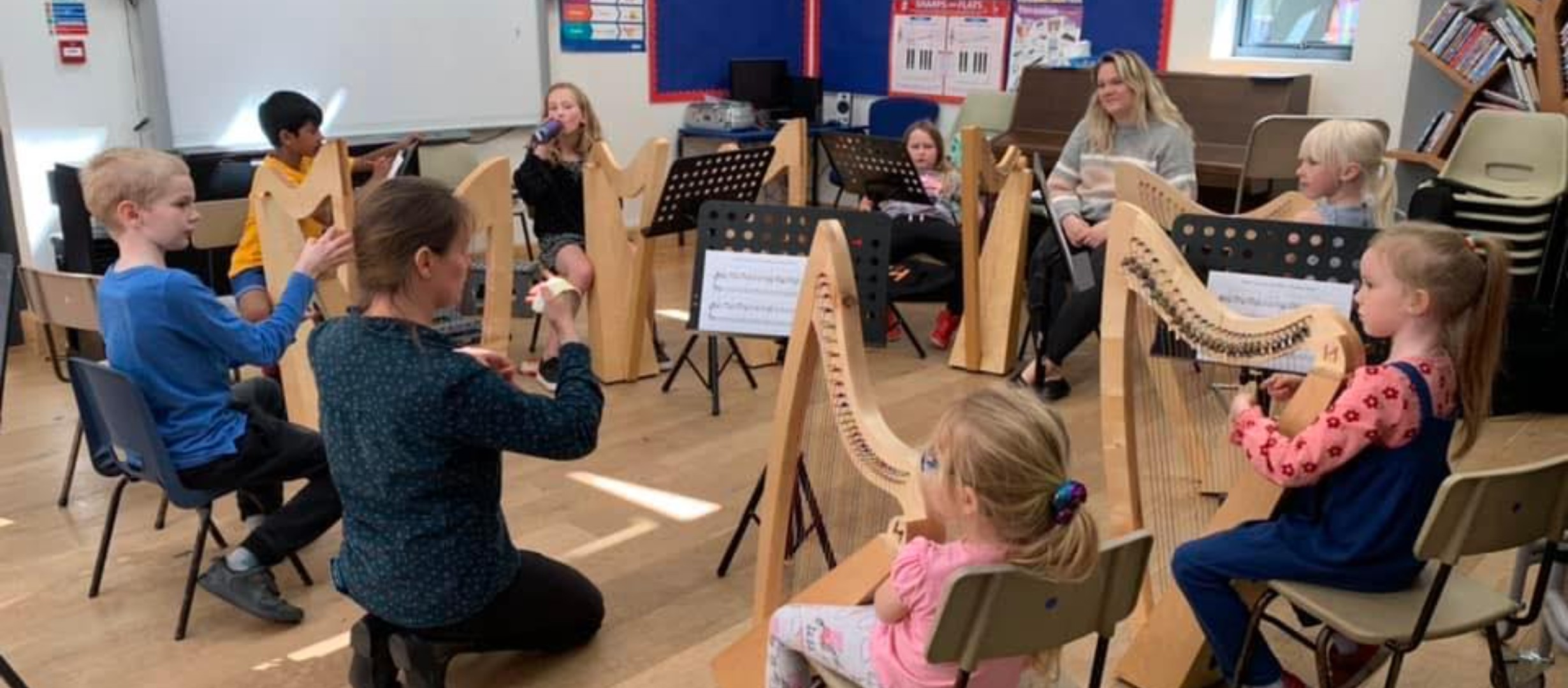 A group of children and adults each holding a harp as the teacher passionately shows them how to play