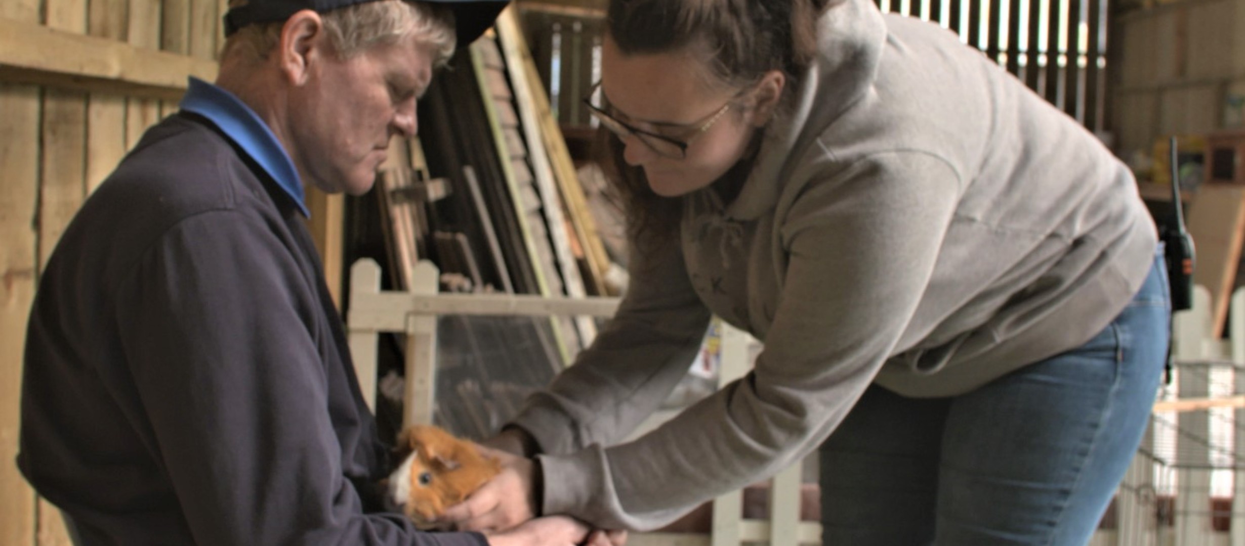 Image shows a man seated with a young woman helping him to hold a guinea pig