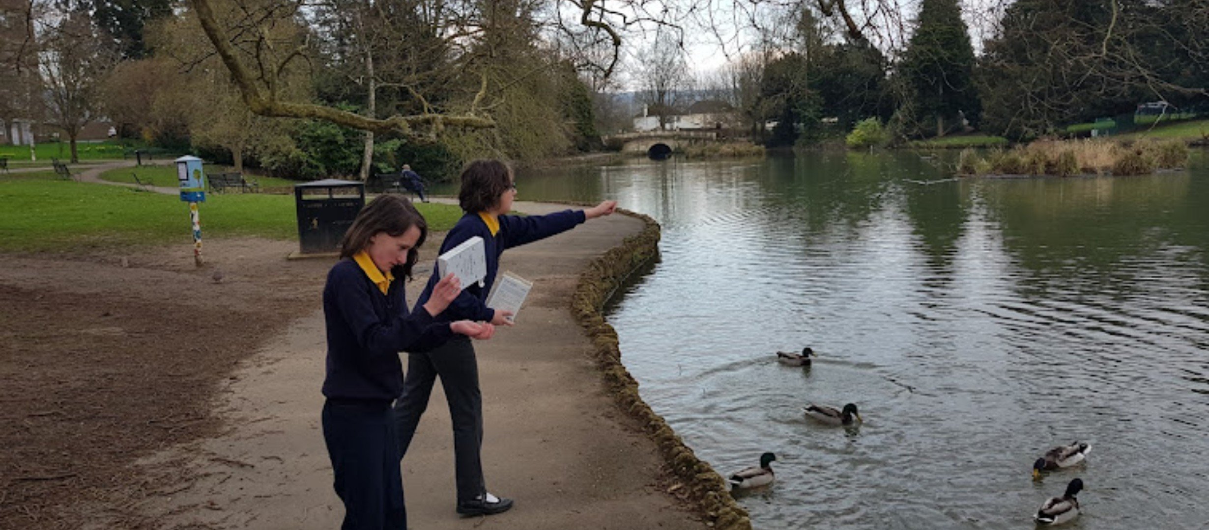 two children throwing food to ducks on a lake