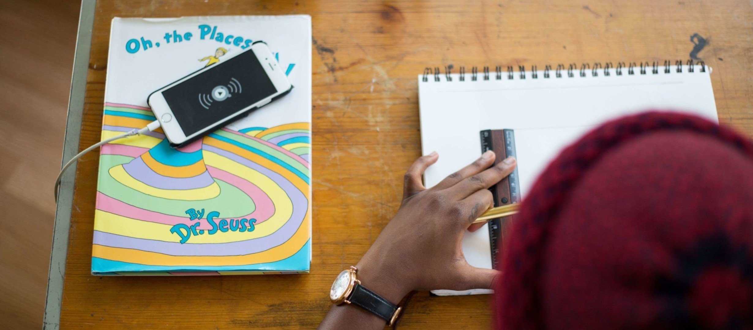teenager sketching on table with pencil and ruler with a phone and book on the table next to him