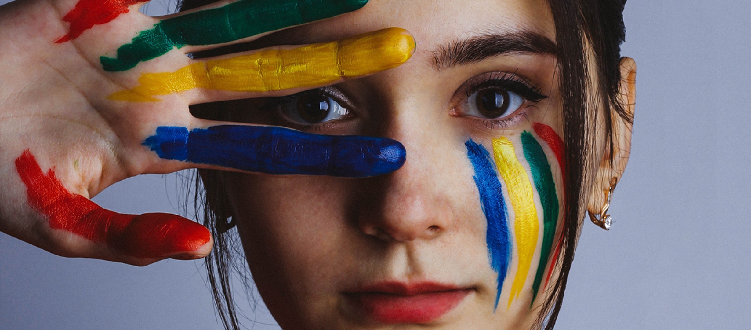 Girl with painted face and hand looking through her fingers