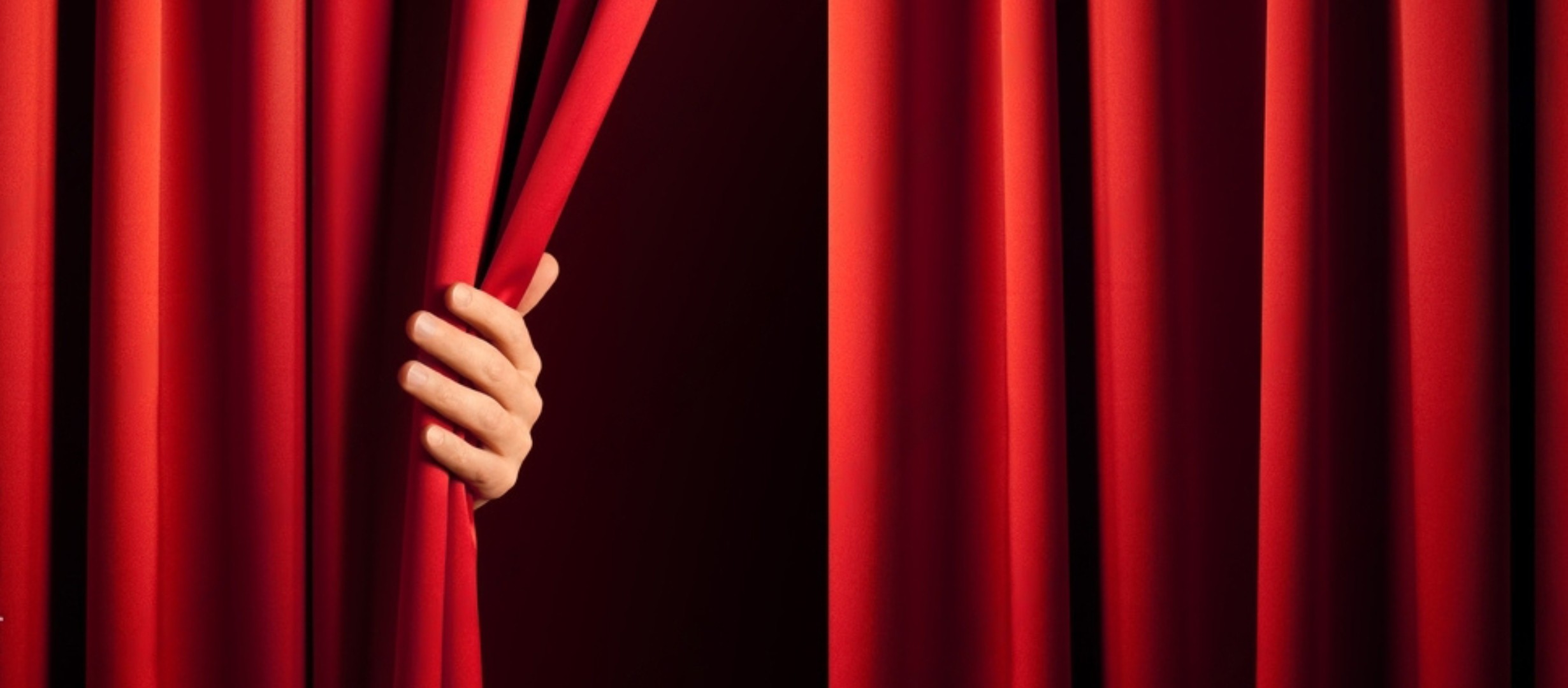 Hand holding back red theatre curtain