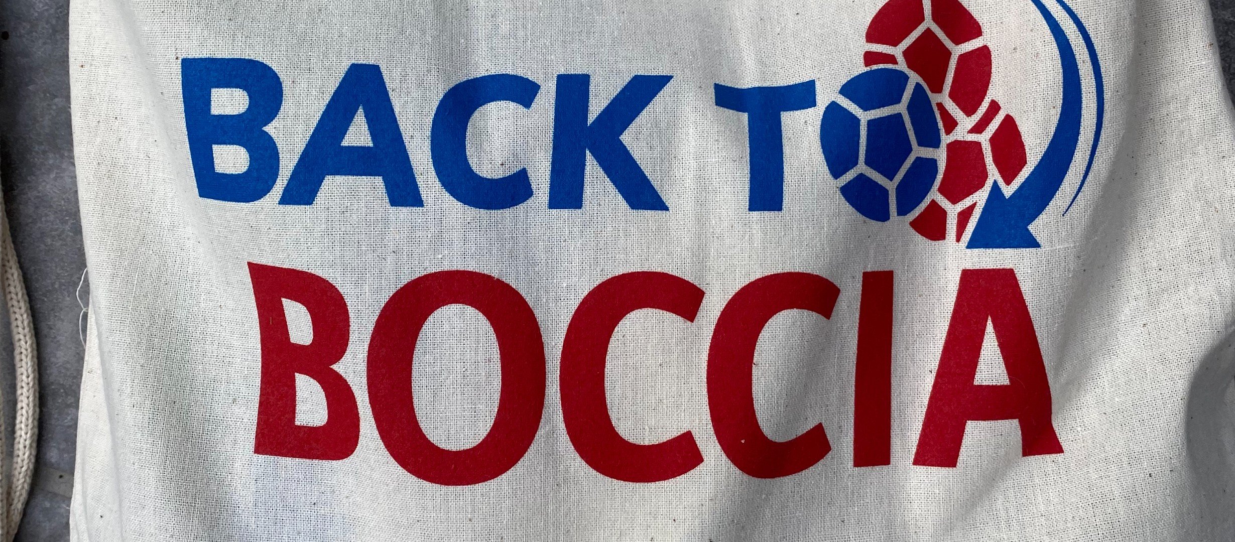 Text printed on a cloth bag reading BACK TO BOCCIA. The 'o' of to is replaced with a boccia ball logo