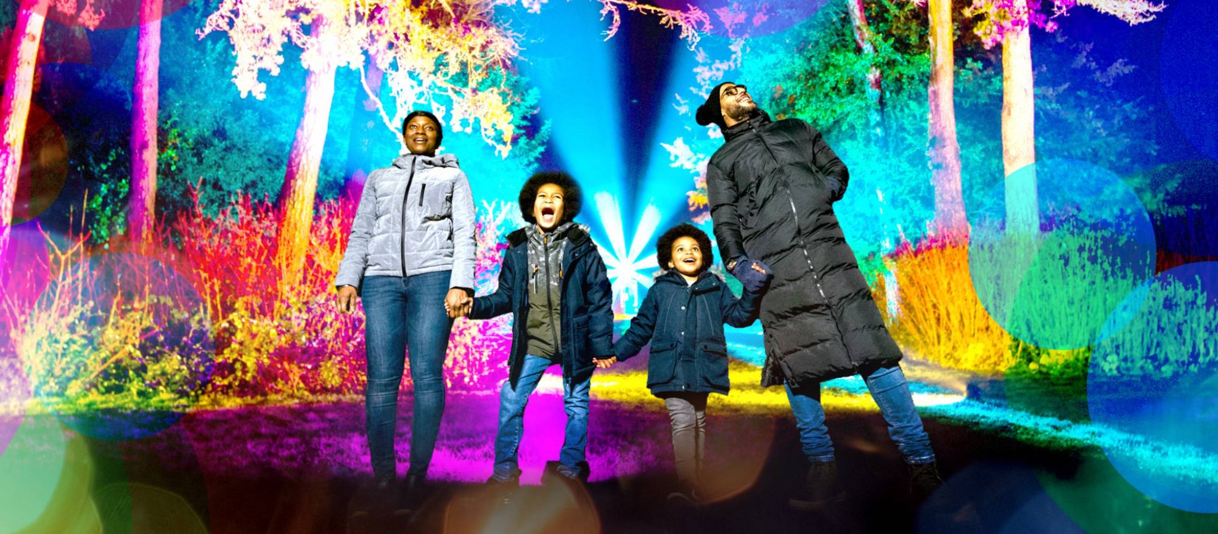 family standing among colourfully lit trees