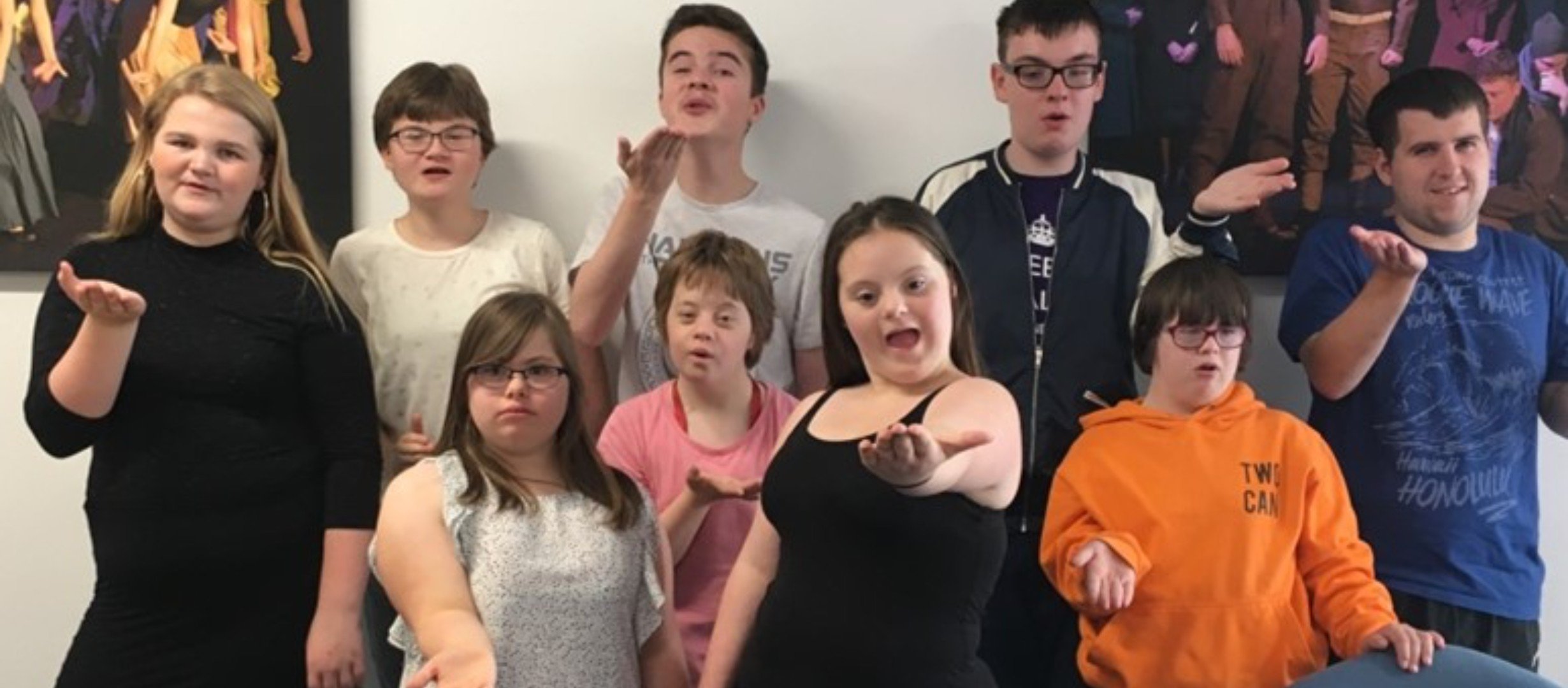 A group of young people all facing the camera all holding one hand in front of them with their palm upturned