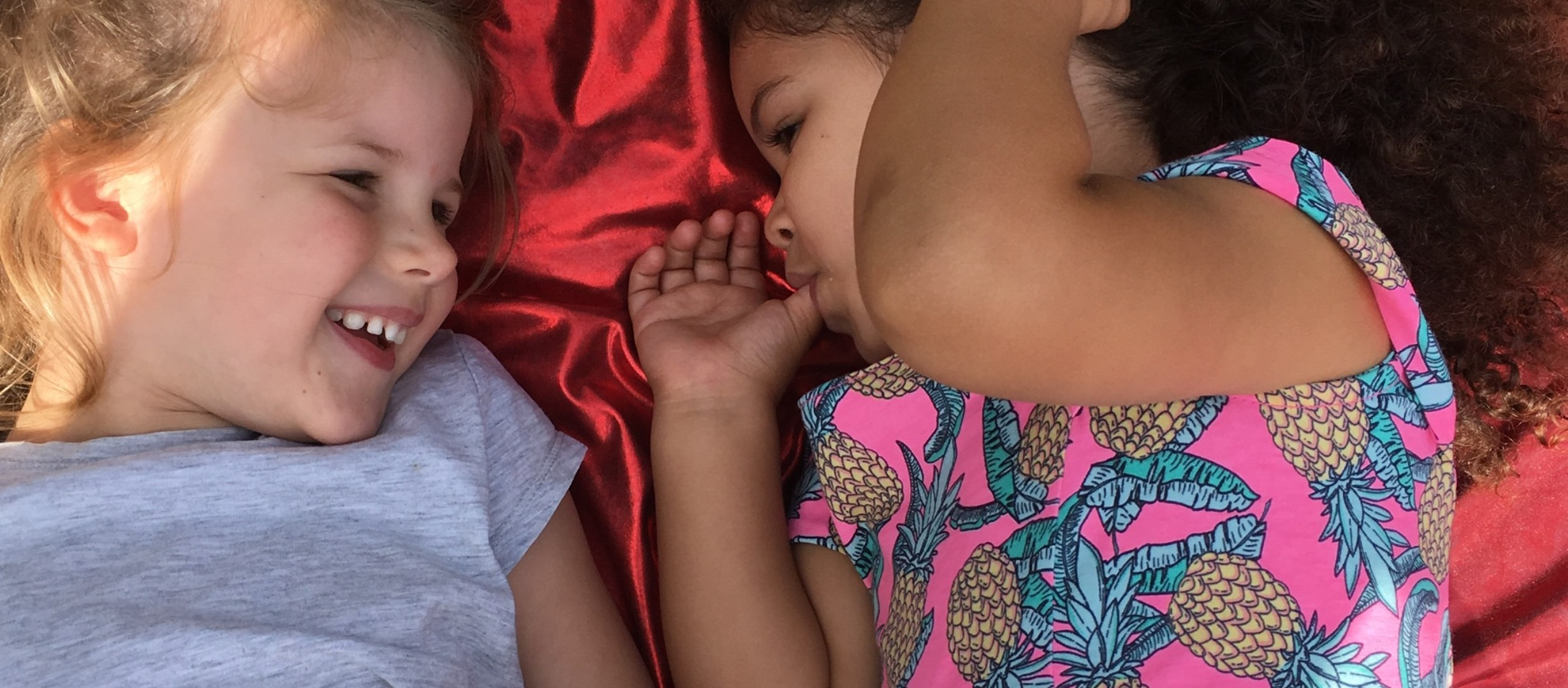 Two young girls lying on a shiny red lycra sheet communicating through smiles in a shared musical experience