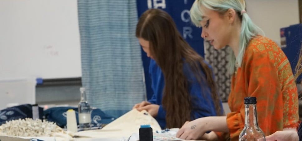 Two women sewing at a table in a studio