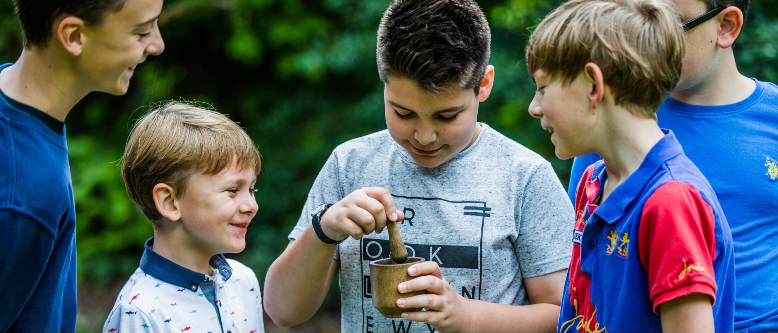 group of children outside with child in centre mixing materials in a pot