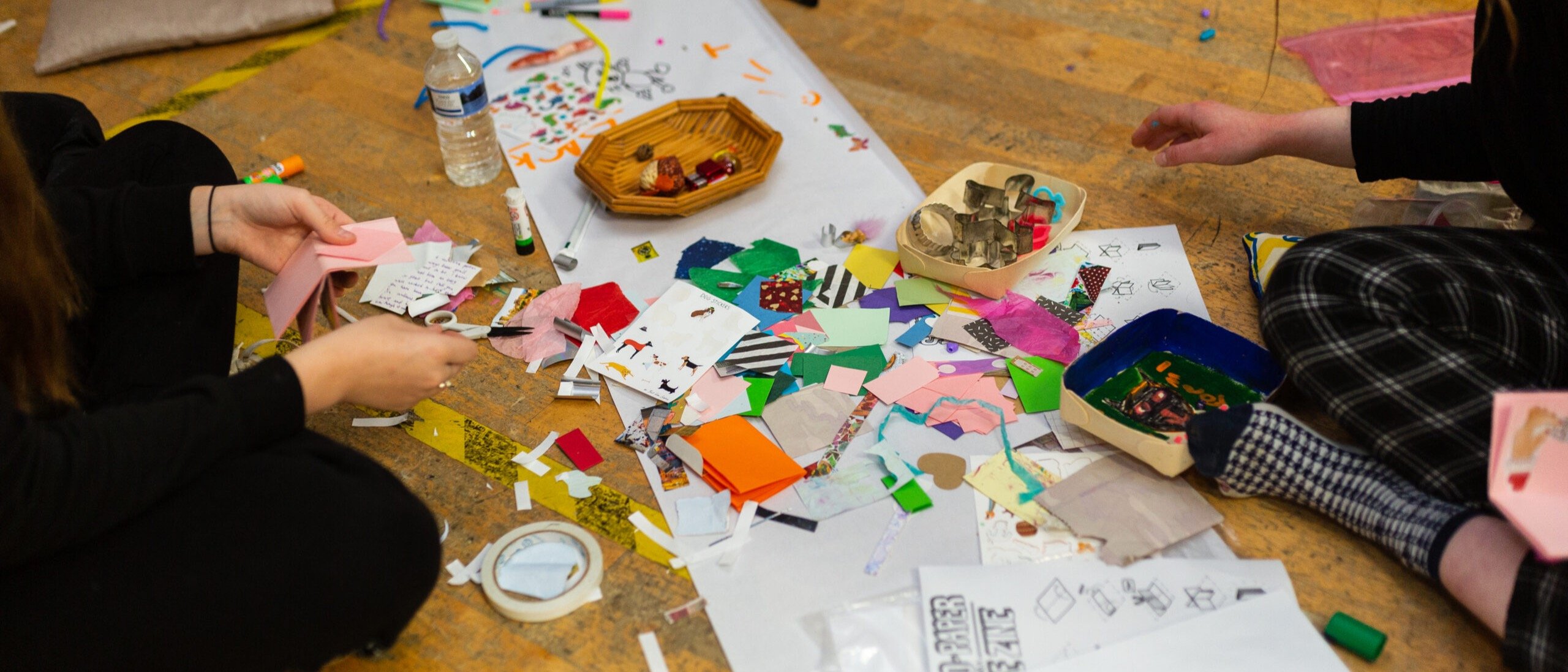 A long strip of paper is stretched out along the floor which is covered in pens, stickers, paper and pencils.