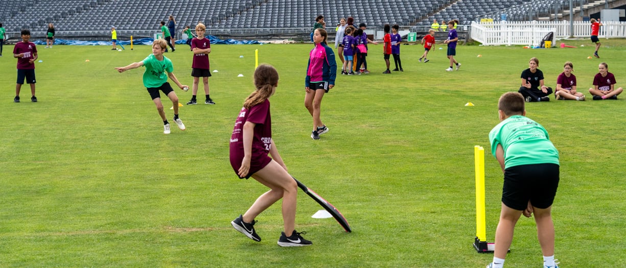 Group of young people in different coloured shirts playing cricket