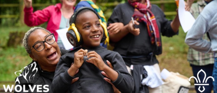 Banner depicting a woman and her child at a scouting event. The child is wearing ear defenders, and has a massive smile on his face.